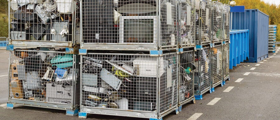 Cages filled with old electronics and appliances, such as monitors and microwaves, stacked in a recycling collection area.
