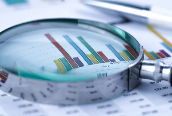 A magnifying glass placed over a printed graph with colorful bar charts, representing data analysis or financial examination.