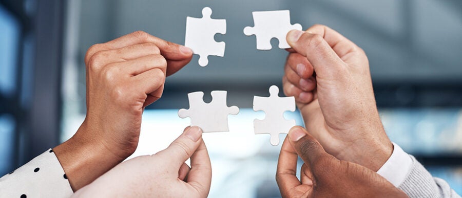 Four hands each holding a puzzle piece, symbolizing teamwork and collaboration.