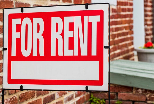 A "For Rent" sign displayed outside a brick building, indicating availability for lease.