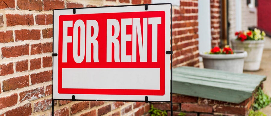 A "For Rent" sign displayed outside a brick building, indicating availability for lease.