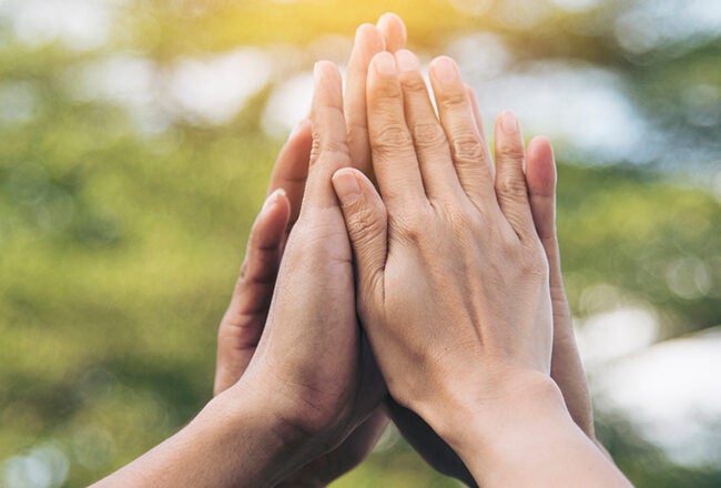 Hands pressed together against a blurred green background, symbolizing unity, support, or teamwork.