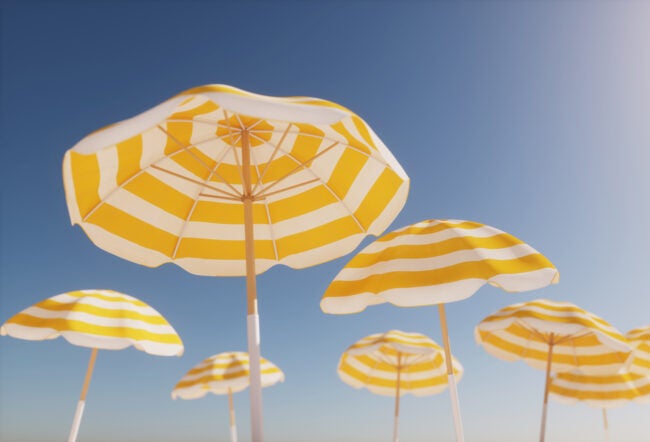 Yellow and white striped beach umbrellas against a clear blue sky, evoking a sunny, summer day at the beach.